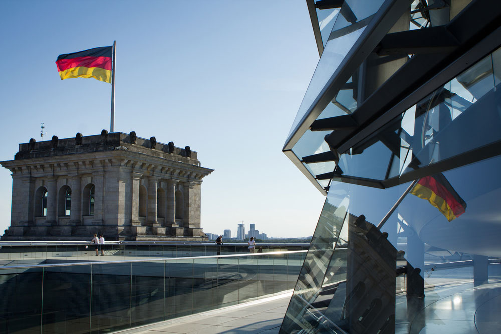 Eine Deutschlandfahne weht auf dem Dach des Reichstages und spiegelt sich im Glas der Kuppel.